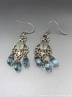 Pair of sterling silver earrings with chalcedony centers and three faceted blue topaz droplet dangles each, shown from front angle.