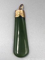 Full view of the jade pendant showcasing its elongate teardrop shape, deep green polished jade and 9ct gold decorated cap with bail.