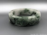 Front view of the jadeite bangle showing the green and white color with detailed carvings of mushrooms and auspicious symbols.