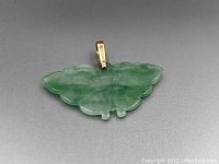 Close-up image of the carved jadeite butterfly pendant showcasing color and translucency with gold bail attachment.