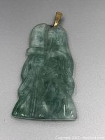 Front view of jadeite pendant showing detailed carving of two embracing figures and gold mount bail