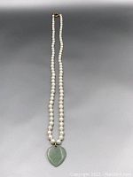 Full view of necklace showing single strand of graduated white pearls with a jadeite heart pendant hanging at the center and a gold clasp at the back.