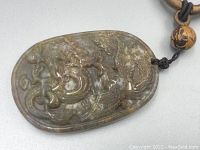 Close-up image showing detailed carving of dragon on the jadeite pendant with visible russet color inclusions and translucency.