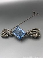 Front view of vintage sterling silver brooch with large square-cut blue topaz stone and marcasite decorated silver wings with safety chain attached.