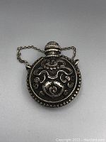 Front-facing view of the round silver Tibetan snuff bottle showing intricate raised ornamental designs and chain attached stopper with turquoise cabochon.