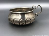 Side view of sterling silver coin dish showing decorative embossed body and handle.