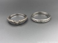 Photo showing two sterling silver rings, one chevron shaped with small clear stones, the other a band with channel set stones.