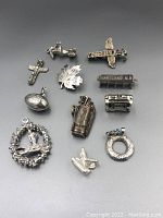 Overview of all sterling silver charms arranged on a gray background, showing different designs and sizes including a maple leaf, golf bag, trolley, cross, wreath, and others.