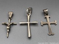 Photo showing all three sterling silver cross pendants laying flat on gray background, displaying their size and design difference.