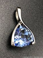 Close-up photo of blue gemstone pendant set in sterling silver, viewed from an angle showing part of the bail and front of the stone.