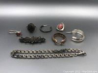 Overview of vintage sterling silver jewellery including rings with varied colored stones, earrings, brooch, and chain link bracelet on neutral background.
