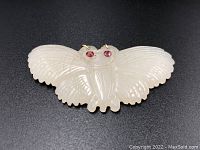 Top view showing the white jade butterfly with carved details, inset ruby eyes, and gold loops.