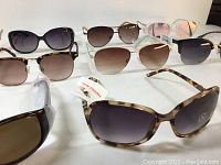 Photo showing 10 pairs of Joe Fresh sunglasses arranged in two rows, featuring different frame colors and lens styles, including tortoiseshell, black, and reflective pink lenses. All appear new and tagged.