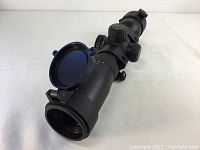 Oblique angle view of the black Excalibur TACT-100 crossbow scope showing flipped open lens cover and adjustment dials.