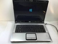 Front view of HP Pavilion dv6000 laptop powered on displaying Windows startup screen with black and silver finish.