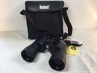 Front view of black Bushnell Powerview binoculars with case, strap, and cleaning cloth on white background.