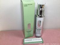 Clinique Even Better Clinical dark spot corrector bottle next to the green box, on a pink surface with a white background.