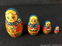 Front view of 4 wooden Russian/Ukrainian nesting dolls arranged by size on black surface