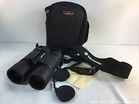 Front view of VANGUARD Sereno binoculars with lens caps, carrying case, neck strap, and lens cloth displayed on white surface.