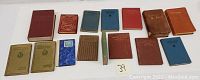 Wide view of 15 19th century books in various colors and sizes laid out on a white surface