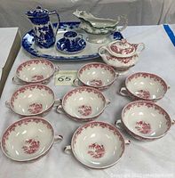 Overall group of serving pieces including blue and white jug and demitasse cup on platter, green gravy boat, lidded pink sugar bowl, and multiple pink soup cups.