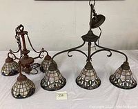 Two vintage Tiffany-style ceiling light fixtures with three slag glass shades each, placed on table for display.