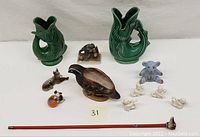 Wide view showing all vintage ceramic figurines including fish pitchers, bird, dog cane, teddy bear bank, angels, dog with ball, and frog on rock figurine.
