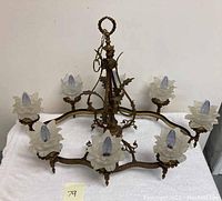 Top and side view of vintage gilt brass chandelier showing seven arms with frosted glass flower-shaped shades and light bulbs fitted.