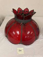 Front view of vintage red slag glass hanging lamp shade sitting on a white cloth surface, showing the rounded petal-shaped glass panels and dark metal frame.