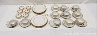 Overview photo of all cups, saucers, plates, and covered bowls arranged on table showing quantity and matching trim design.