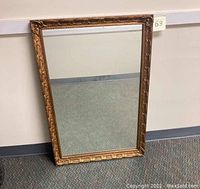 Full view of the rectangular vintage gold gilt wall mirror with ornate carved frame leaning against wall.