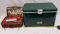 Green vintage Thermos metal cooler and picnic kid plastic set in a wicker basket with metal Thermos bottle and red cups