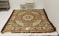 Photo showing the full woven tapestry blanket laid flat on floor with two white wicker nesting tables placed behind it.