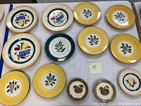 Photo showing 11 vintage Stangl Pottery fruit plates with various fruit designs on ceramic plates with colorful rims in yellow, green, and cream.