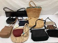 Overall view of 11 handbags on white surface, includes leather, straw, fabric styles in various colors and sizes.