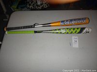 Two aluminum baseball bats on a table, one Easton orange and black, one Louisville Slugger black, green, and white.