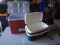 Two large coolers; one red with a split lid and four drink holders, one green with a white lid.