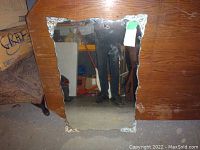 View of sculpted edge mirror leaning against wooden piece of furniture showing molded corner decorations and irregular edge shape.