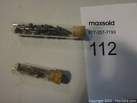 Two corked glass tubes filled with small metal watch parts and stems on flat surface with lot number paper
