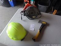 Photo of the yellow hard hat, axe with yellow and black handle, and Black & Decker electric circular saw on white table.