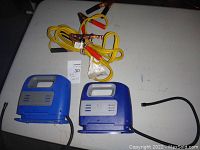 Two blue automotive air machines and coiled yellow booster cables with copper clamps on a white surface.