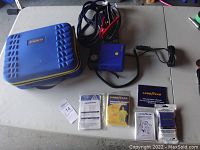 Overview photo showing the closed blue zippered carrying case along with emergency supplies including gloves, safety triangle, and pamphlets.