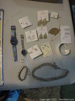 Full view of all jewelry items and wristwatches laid out on a flat surface including earrings, bracelets, necklaces, and two watches.