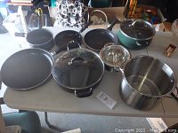 Overview of all pots and pans on table showing various sizes and types of cookware including frying pans, saucepans, stockpot, glass lids, and steamer insert.