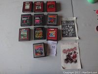 Lot of 10 Atari 2600 game cartridges laid out with two manuals visible for Jr. Pac-Man and Q*bert games.