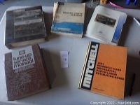 Lot of six various used car repair manuals including a brown tune-up service manual, blue and white Studebaker parts manual, a Ford fleet guide, and a large orange Mitchell estimating guide.