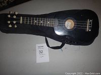 Full view of black Magic ukulele resting on the soft black carrying case, showing the whole instrument and case.