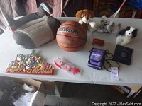 Full view of all items on the table including booster seat, basketball, three plush animals, Gameboy pouch, Mickey Mouse Christmas plaque, red device, and blue booklet.