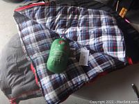 Sleeping bag spread out showing plaid lining with green mosquito shelter sack and informational tags on top.