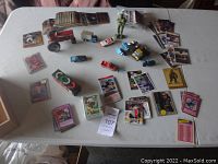 Table containing various sports cards, Yugioh cards, toy vehicles including a diecast tractor, green action figure, and a Rubik's Cube puzzle.